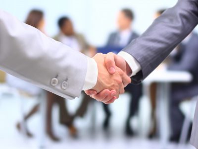 Two successful businessman shaking hands in front of corporate team at office
